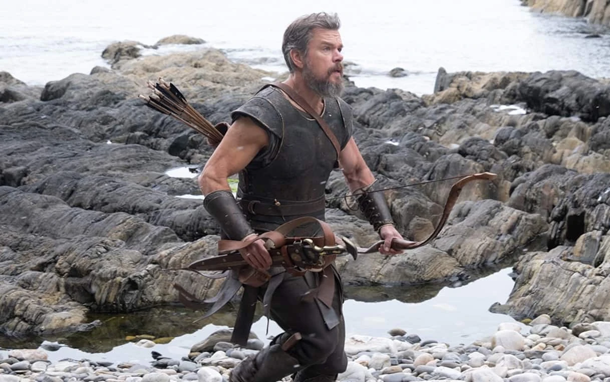 Matt Damon nei panni di Ulisse con arco e faretra su una costa rocciosa