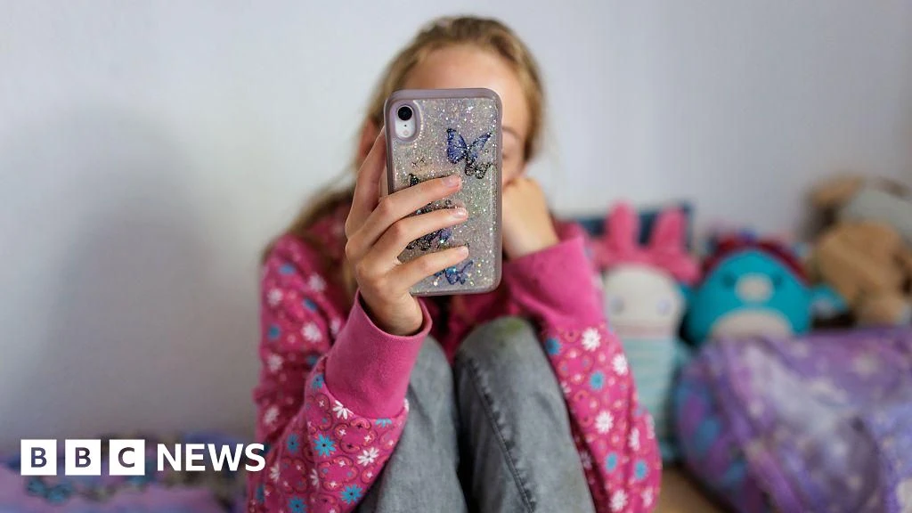 Una ragazza usa uno smartphone in camera, immagine BBC News su sicurezza online dei minori
