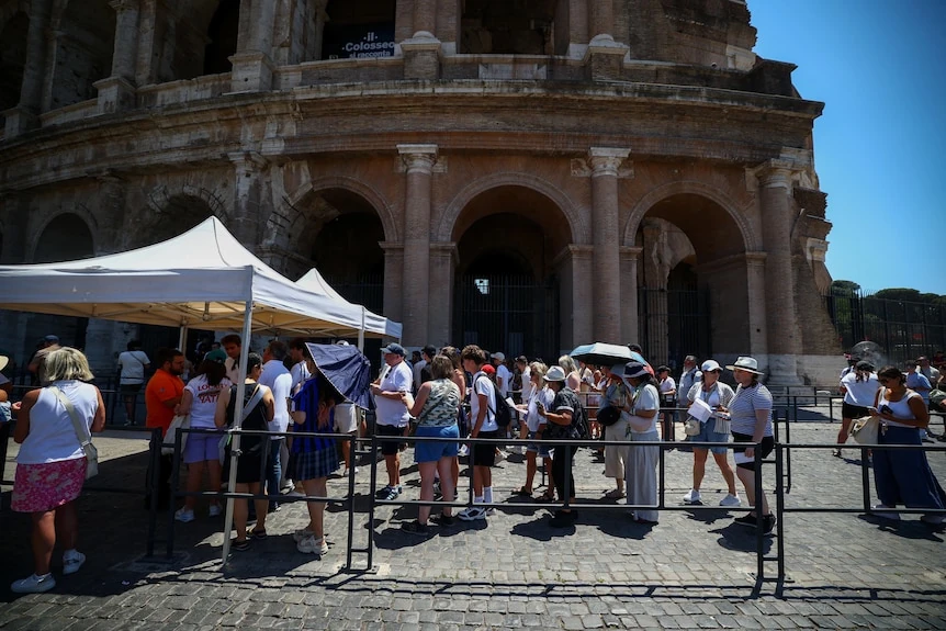Turisti in fila sotto il sole davanti al Colosseo, riparati da ombrelli e cappelli