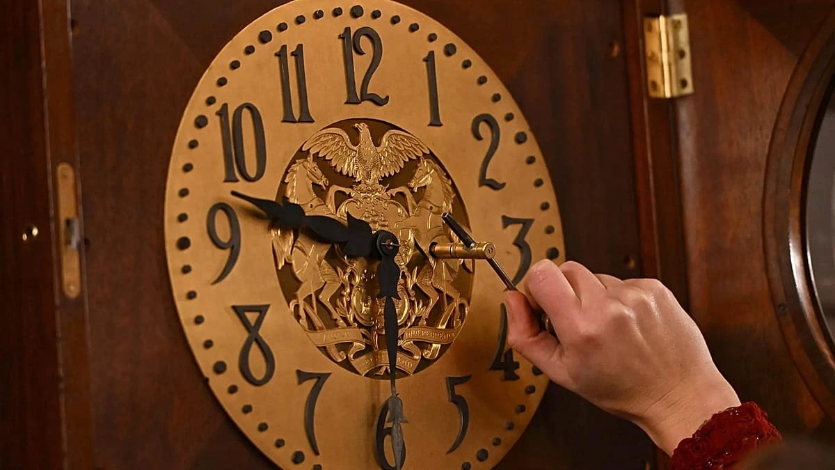 Una mano regola le lancette di un vecchio orologio a pendolo