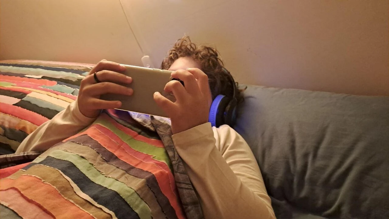Adolescente sdraiato sul letto con cuffie che guarda lo smartphone