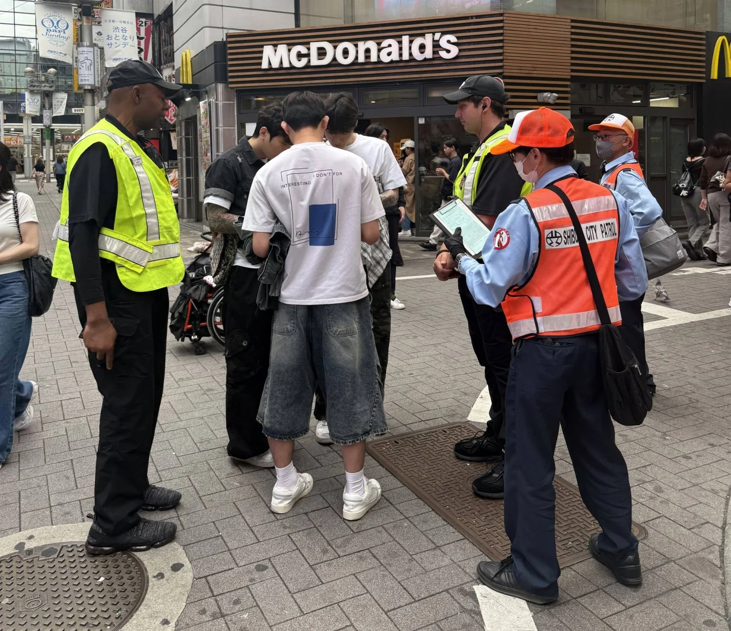Addetti della pattuglia di Shibuya elevano una multa a un giovane davanti a un McDonald's a Tokyo