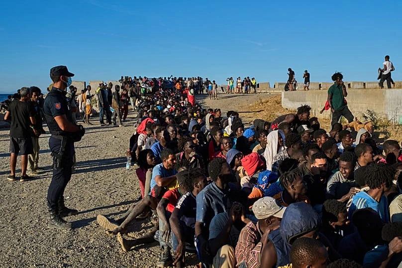 Migranti in fila per la distribuzione di cibo su una spiaggia di Ceuta, 3 agosto 2026